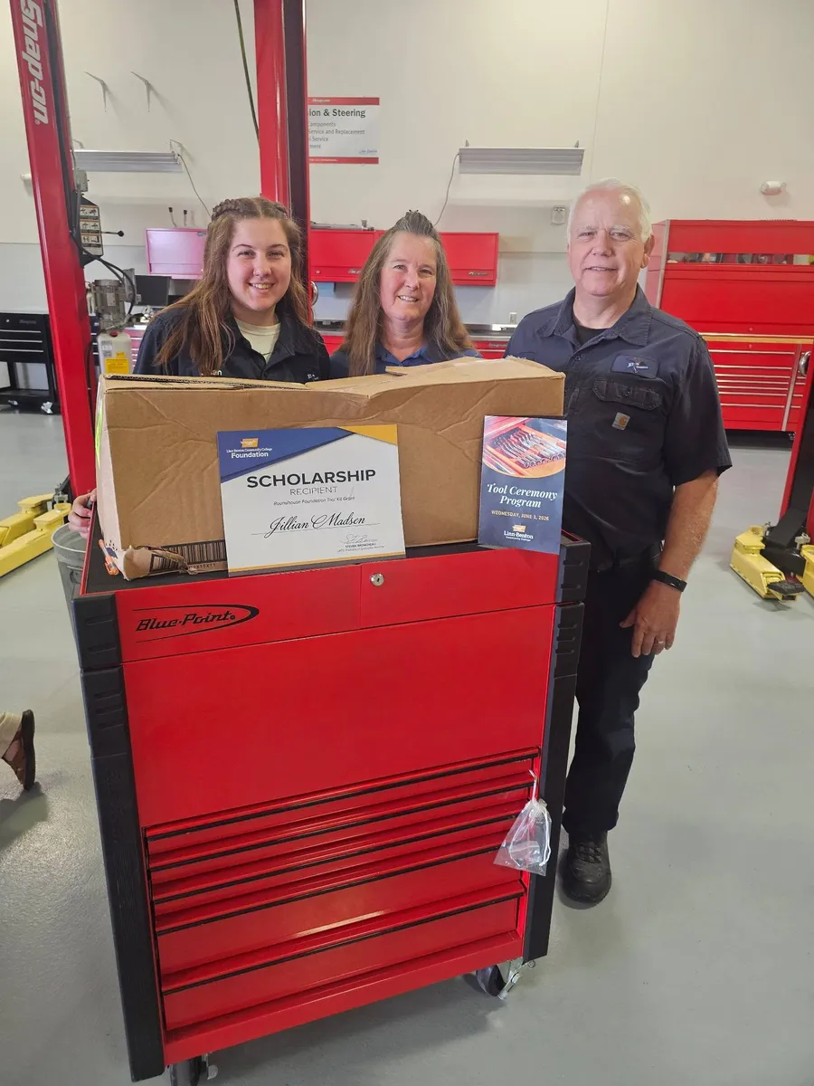 Jillian holding her scholarship certificate on a new red tool chest, with Russ beside her